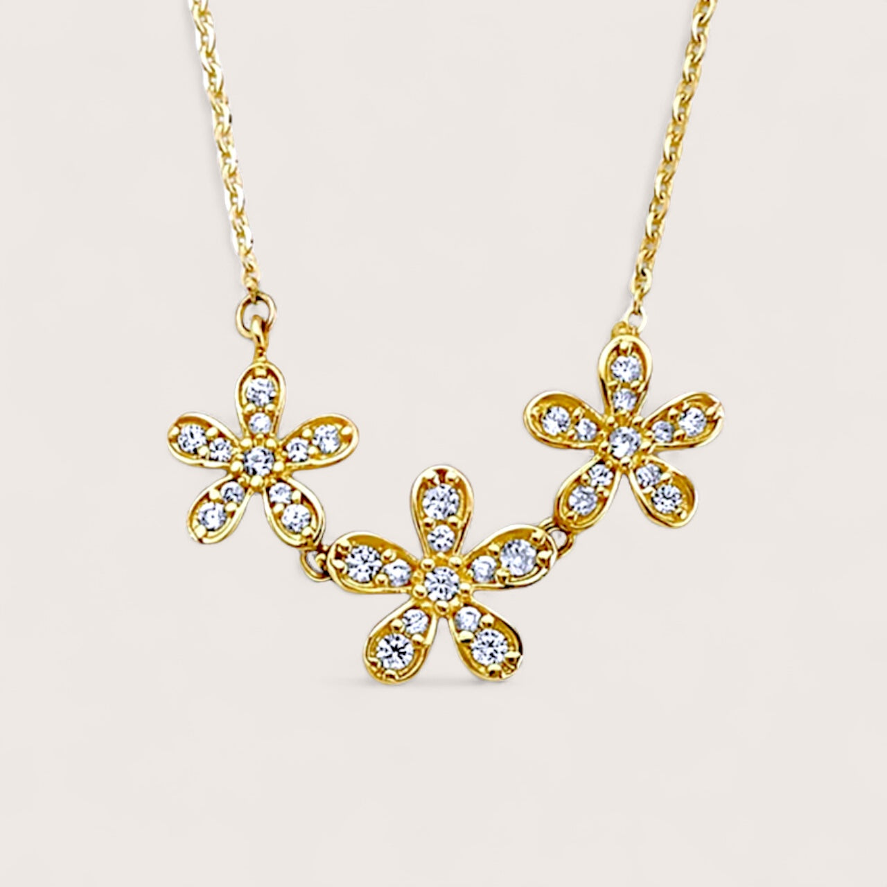 close up of Gold necklace with floral pendants on a light beige background