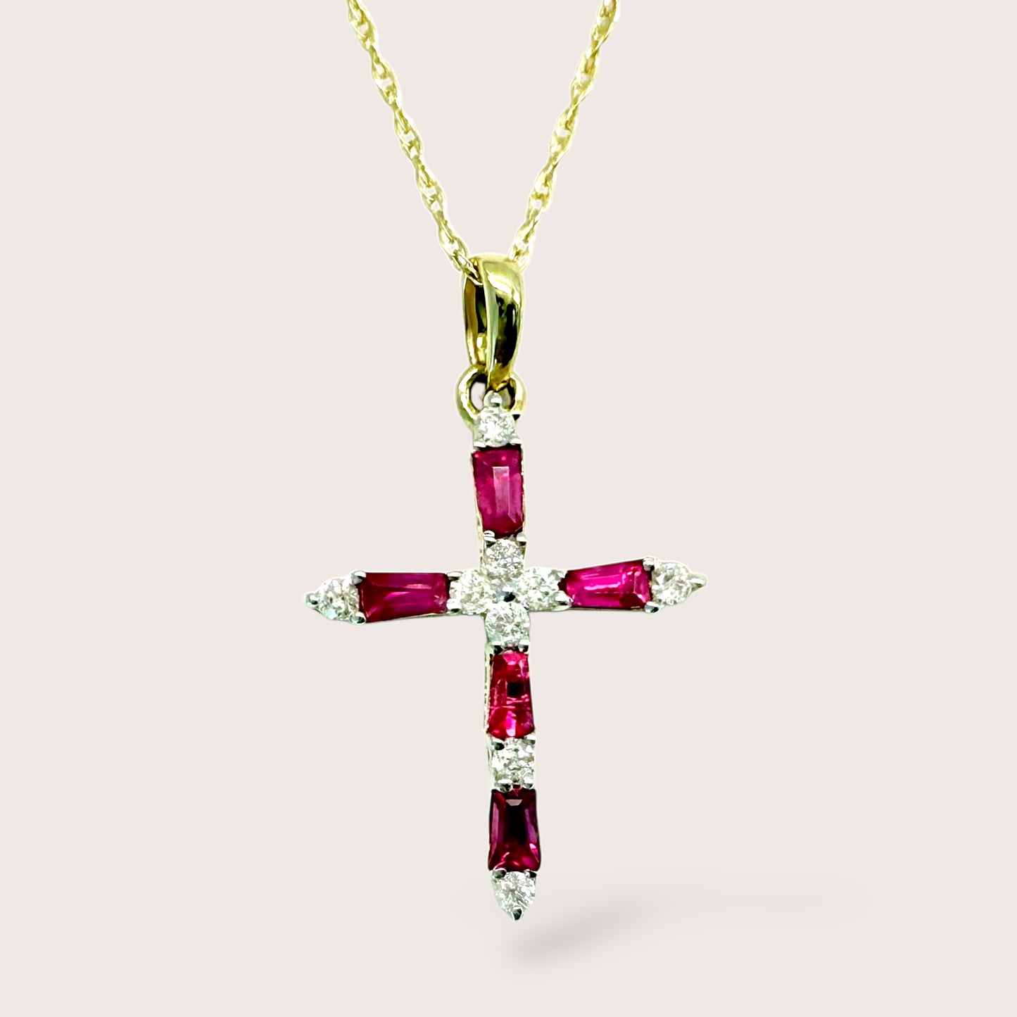 Gold cross pendant with red gemstones and clear stones on a light pink background