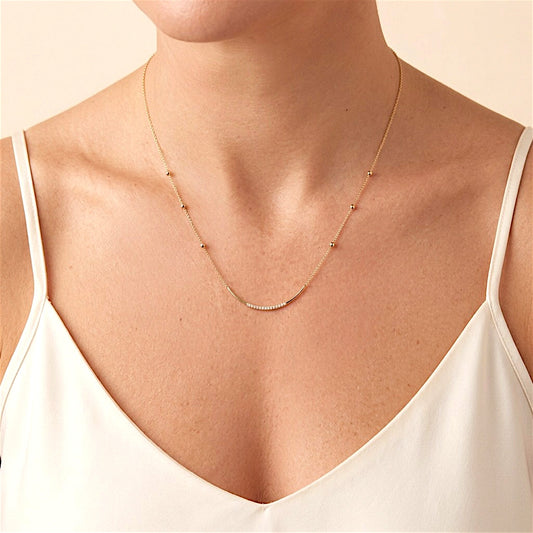 Gold bead-station necklace with a curved CZ bar worn at the neckline above an ivory camisole
