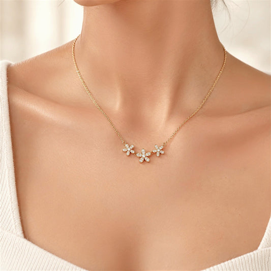 Three-flower gold CZ necklace worn at the neckline above an ivory ribbed top