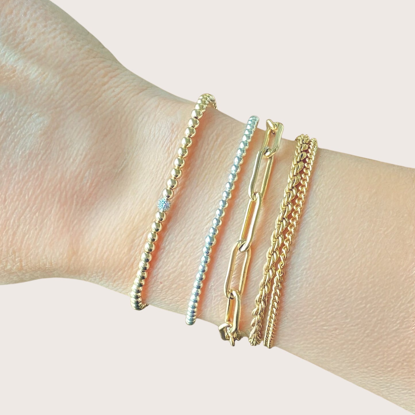 14K Gold Beaded Diamond Bracelet shown on a models wrist stacked with other gold bracelets