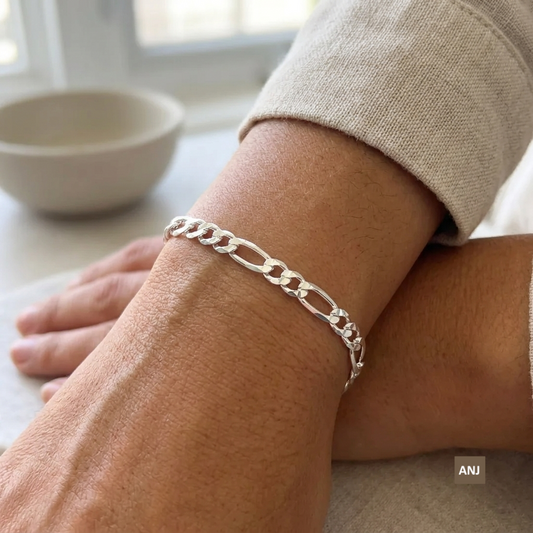 A close-up lifestyle shot showcasing the 4mm unisex sterling silver Figaro chain bracelet worn elegantly on a wrist, demonstrating how the links lay perfectly flat against the skin.