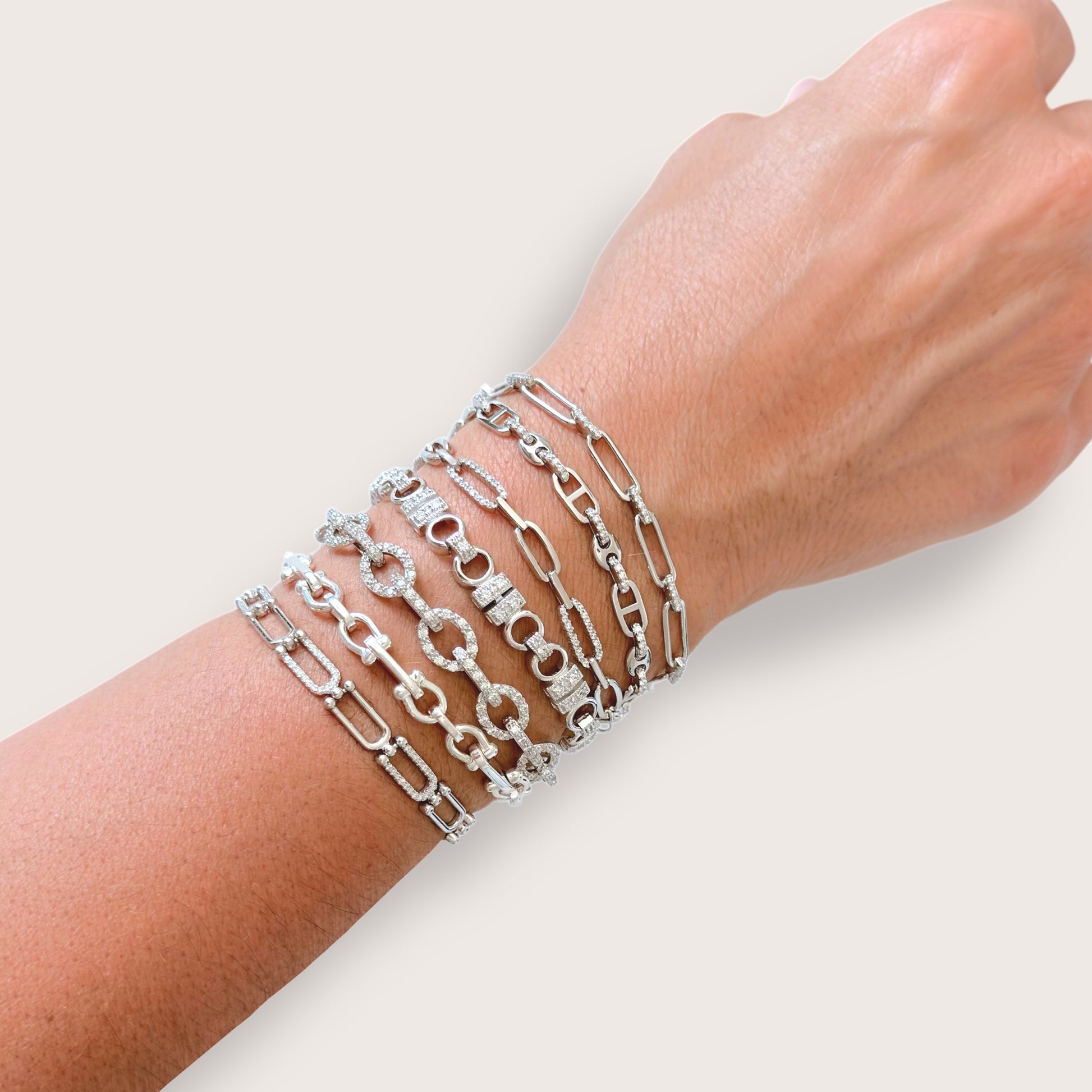 Silver chain bracelets stacked on a wrist against a light background