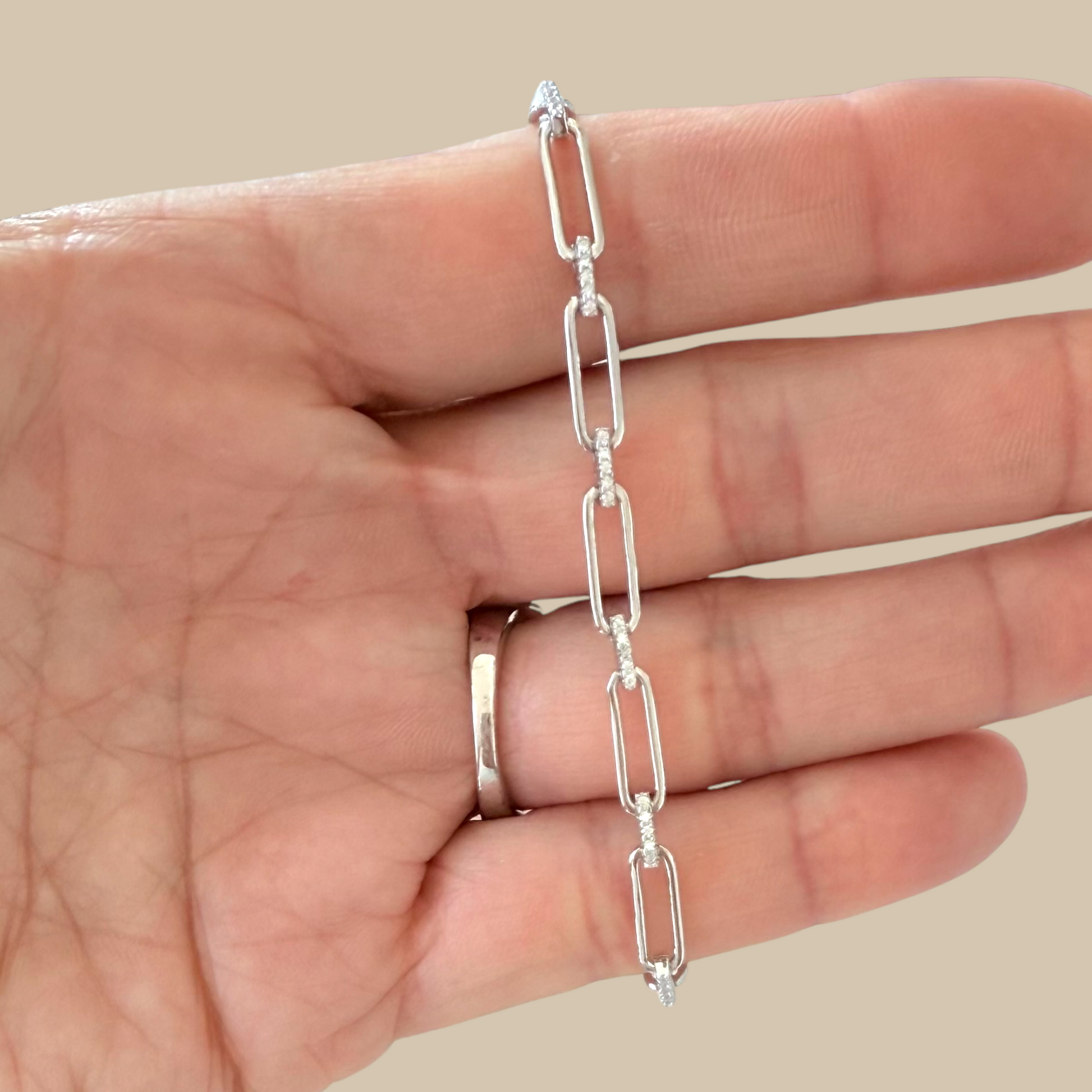 Silver chain necklace held on a hand against a beige background