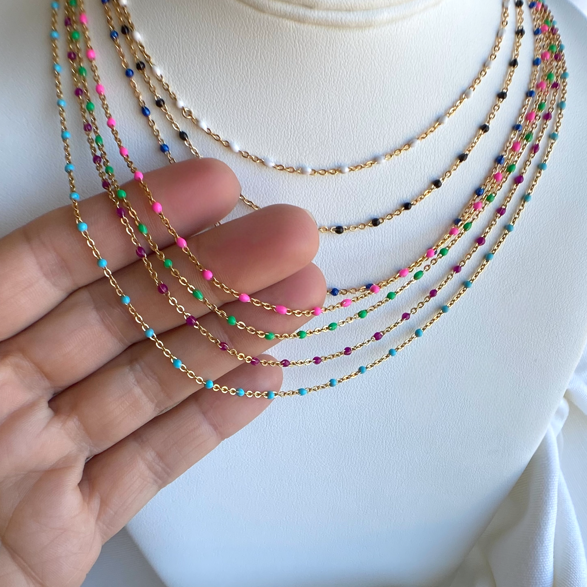 Colorful beaded necklaces on a mannequin with a hand holding one necklace.