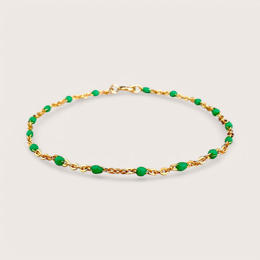A dainty gold bracelet with emerald green enamel beads on a chain design, displayed against a plain background.