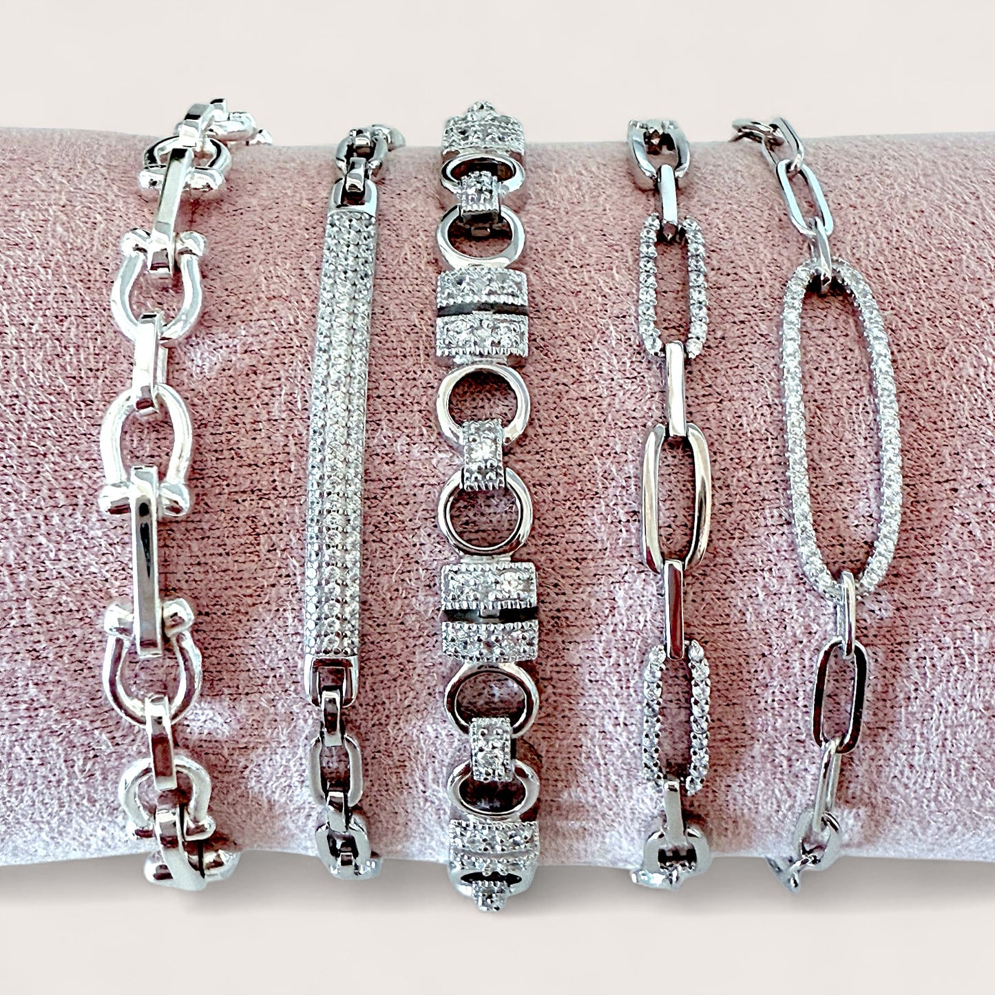 Five silver bracelets of different designs on a pink surface