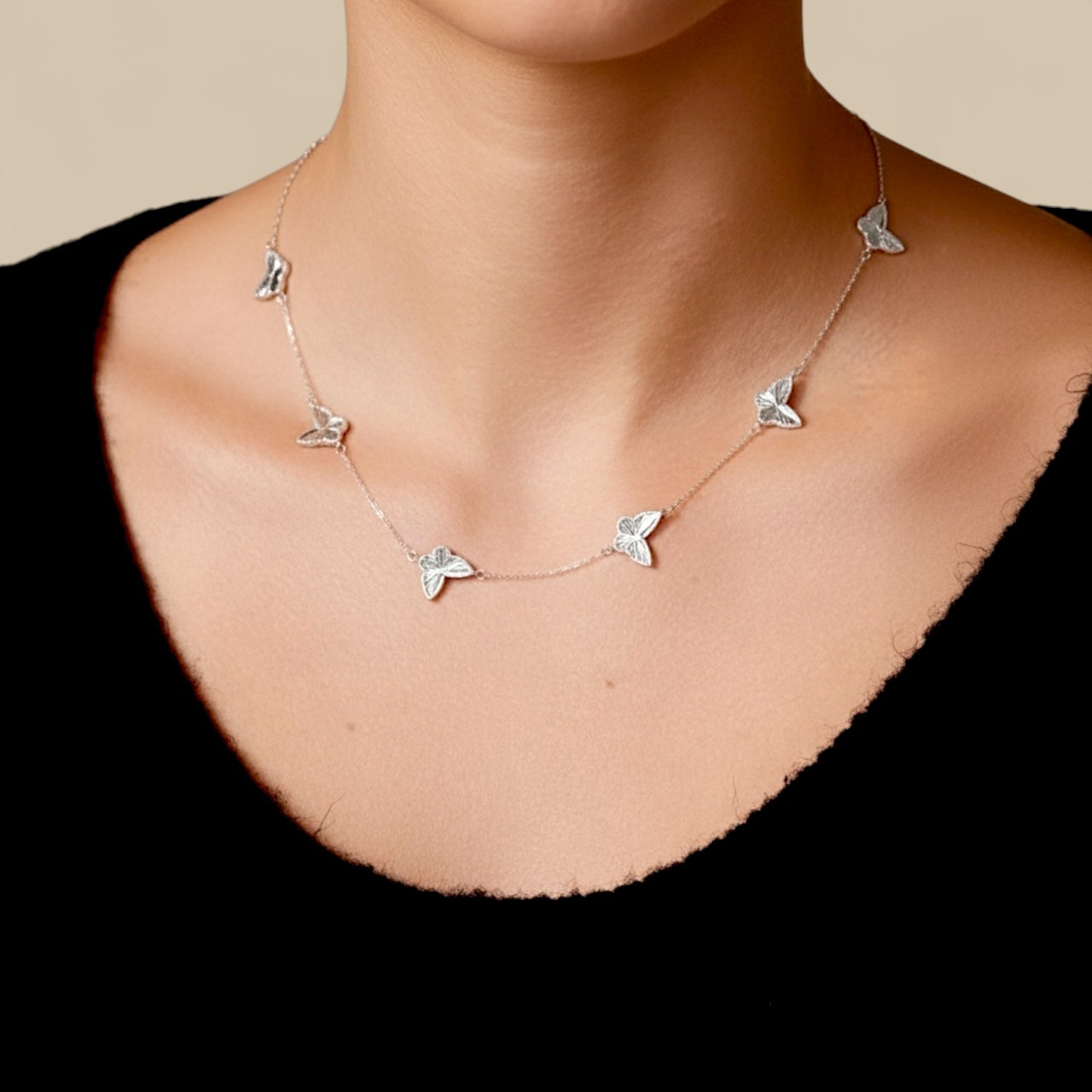Rhodium Sterling Silver Necklace with 6 faceted diamond cut butterfly pendants stationed evenly across a delicate silver cable chain on a person wearing a black top