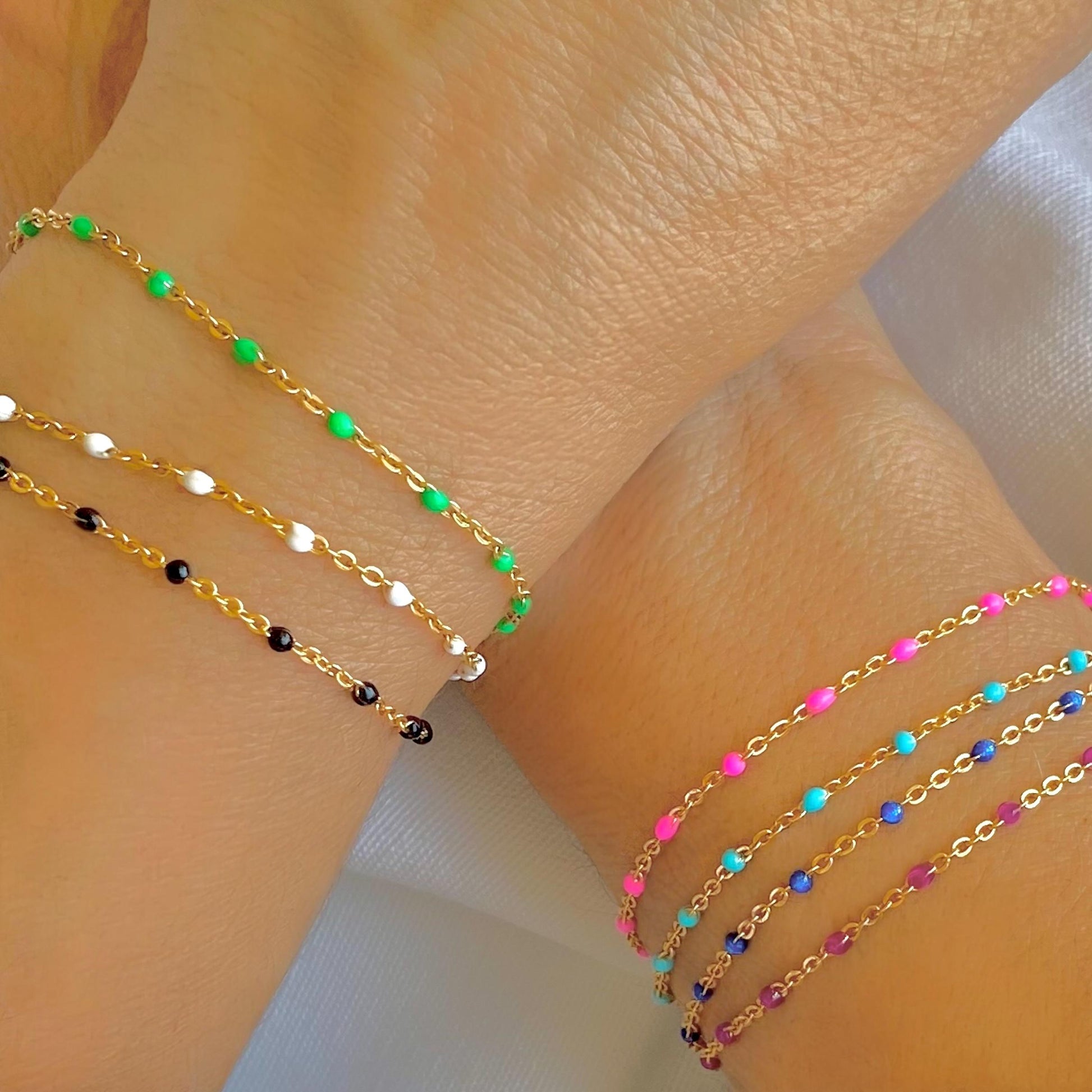 Two wrists adorned with gold-colored enamel beaded chain bracelets in vibrant colors.