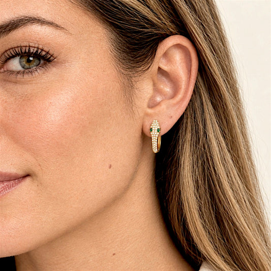 Close-up of a lighter-haired model wearing a gold pavé snake huggie hoop with green zircon eyes in her first lobe piercing.