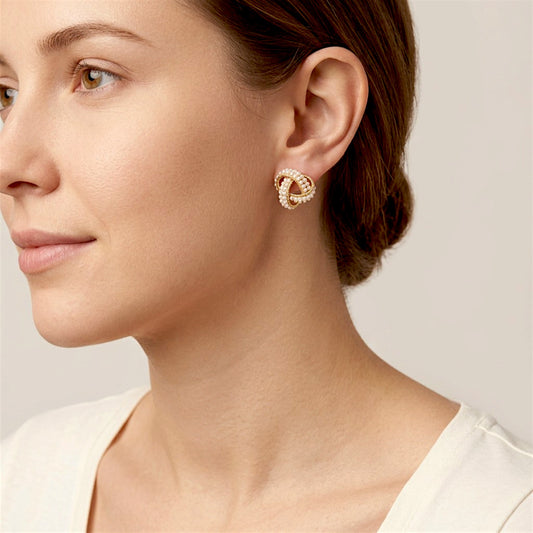 Woman with brown hair swept back wearing a pearl-covered gold love knot stud earring and an ivory top.