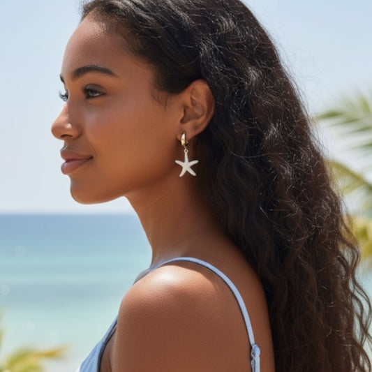 Woman wearing gold starfish dangle earrings with a beach background
