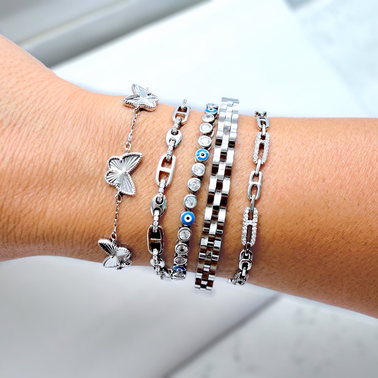 Wrist wearing multiple silver bracelets with butterfly and chain designs on a light background