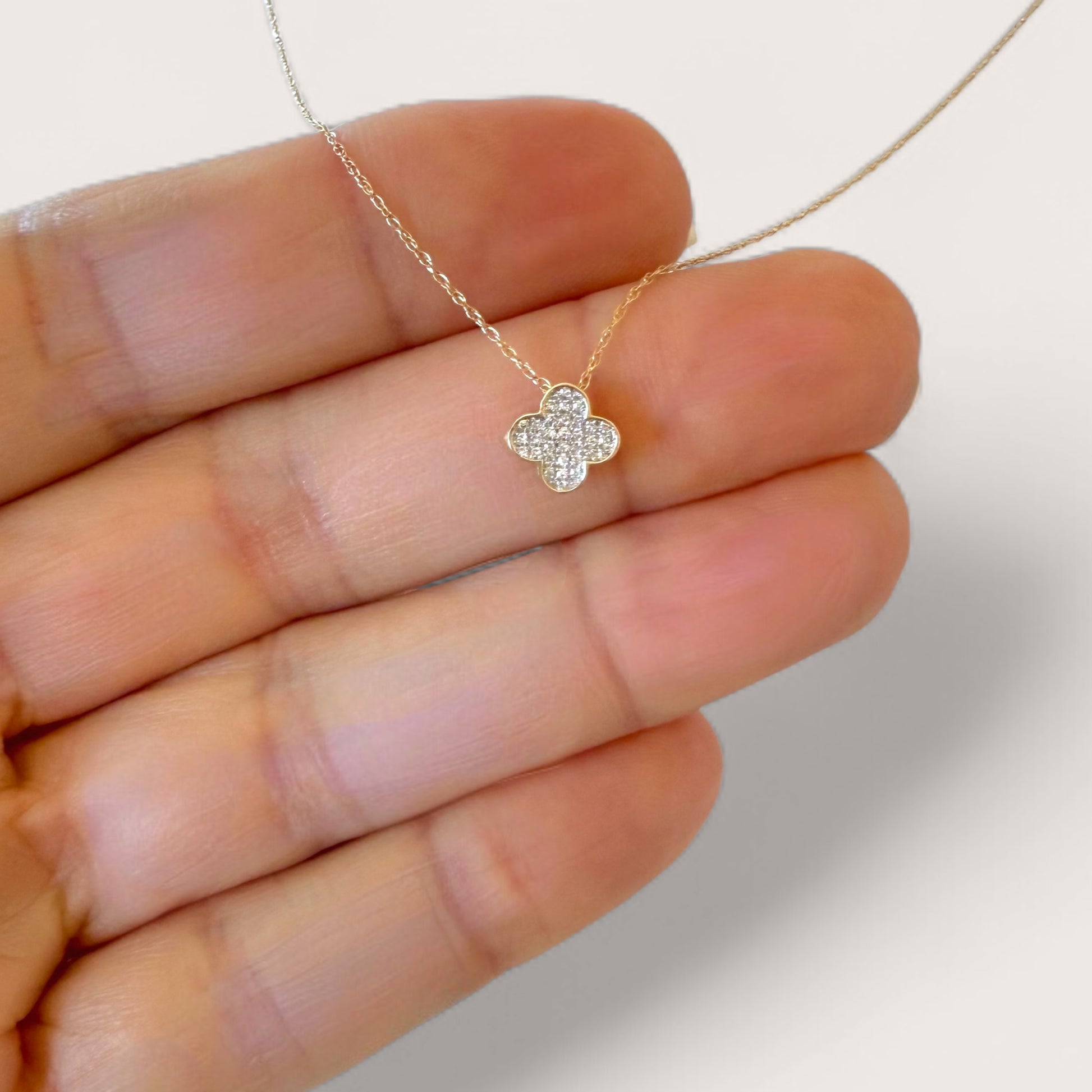 Gold necklace with a clover-shaped pendant held between fingers against a neutral background