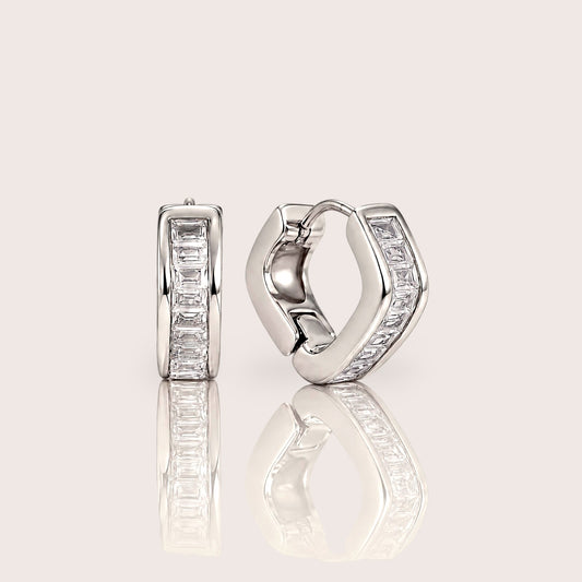 Silver-tone hex baguette huggie hoop pair shown from the front and side on an ivory surface with soft reflections.