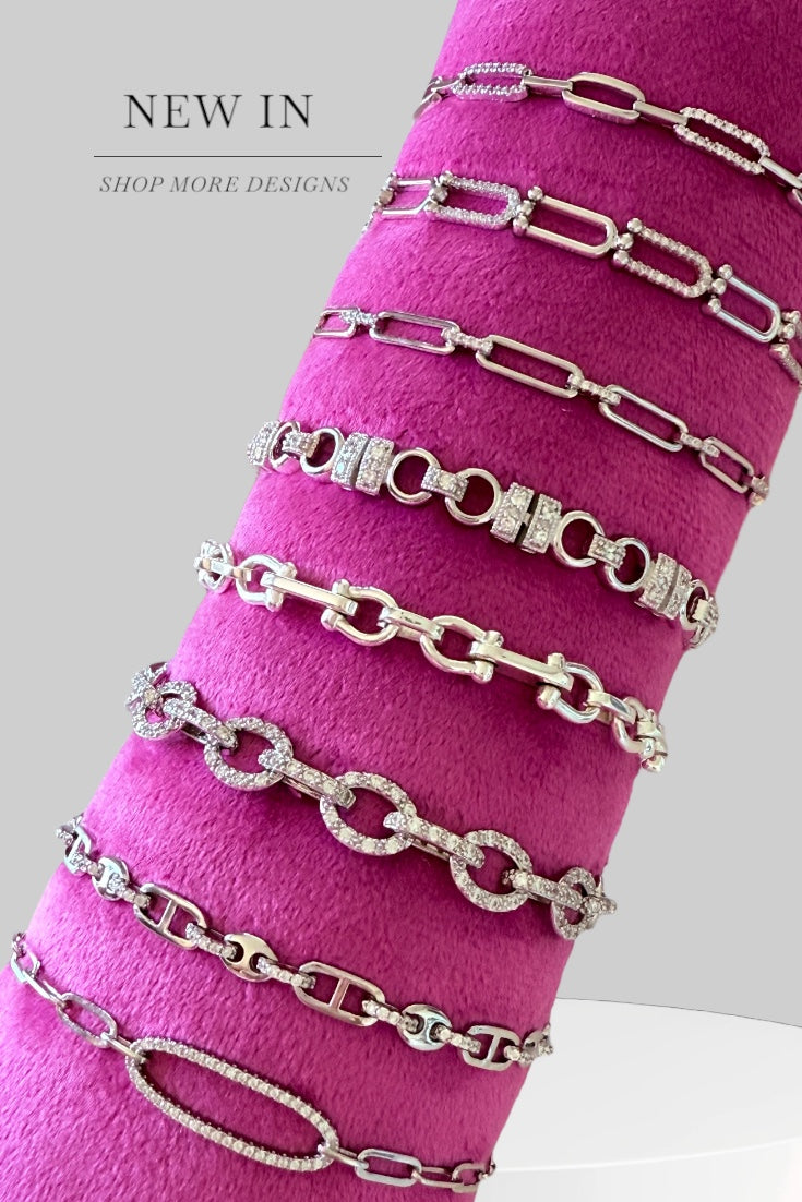 Collection of silver chain bracelets on a pink surface with text 'NEW IN' and 'SHOP MORE DESIGNS'.