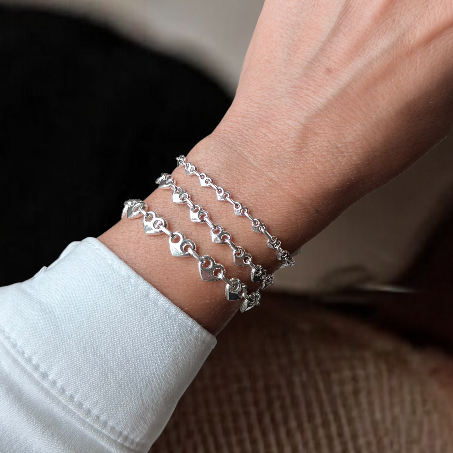 Silver bracelet with heart-shaped links on a wrist against a neutral background