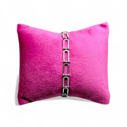 Silver bracelet on a pink pillow with a white background