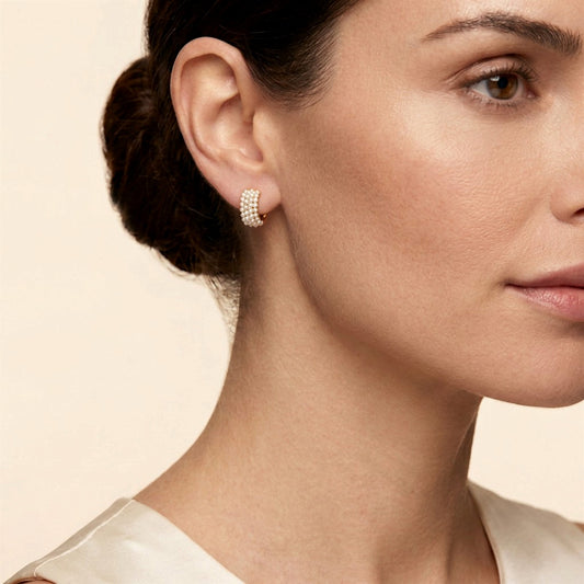 Woman wearing a gold freshwater pearl cluster huggie earring, showing its fit against the earlobe.
