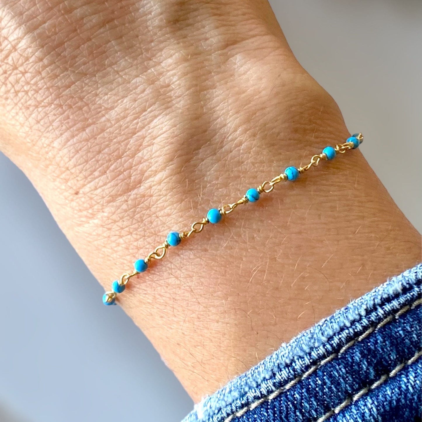 A turquoise bead bracelet with a gold chain, displayed on a wrist. 14k Gold plated Serling Silver Turquoise Beaded Chain Bracelet