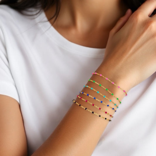 Minimalist wrist stack featuring the pink enamel satellite chain bracelet stacked with classic gold colorful bracelets in 14K yellow gold filled by Ashley Nicole Jewelry.