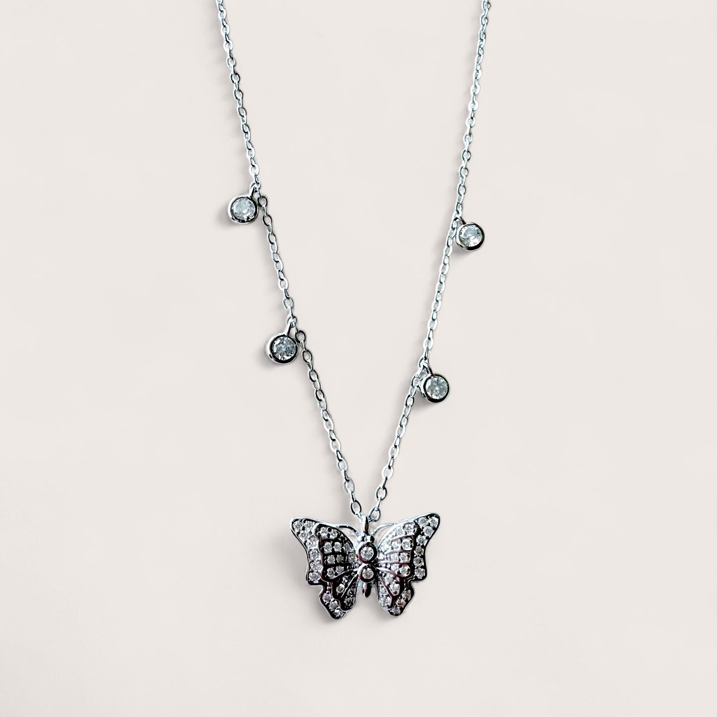 A sterling silver necklace with a 3D butterfly pendant adorned with cubic zirconia gems, with additional small bezel set stones on a chain.