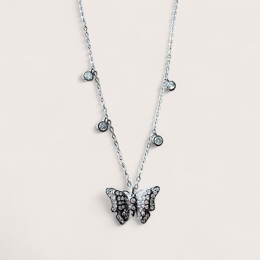 A sterling silver necklace with a 3D butterfly pendant adorned with cubic zirconia gems, with additional small bezel set stones on a chain.
