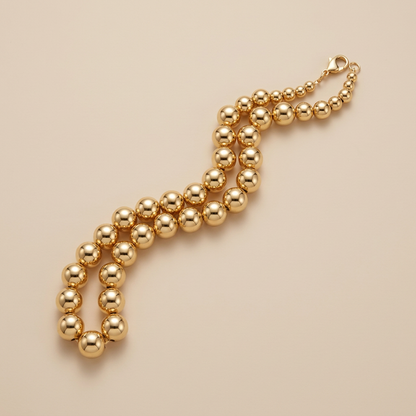Gold-filled bead necklace folded on a beige background, showing graduated end beads and lobster clasp