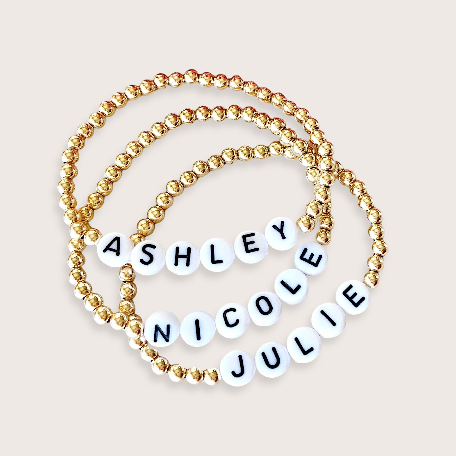 A gold-colored beaded bracelet with personalized engraved names 'Ashley Nicole' on it, showing a series of round beads strung on an elastic cord.