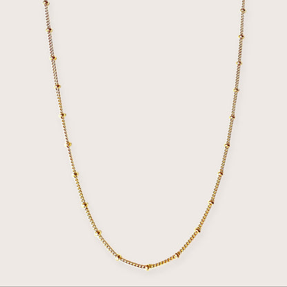Vew of a 14K gold-filled beaded satellite station necklace featuring delicate curb chain links and evenly spaced round station beads against a neutral background
