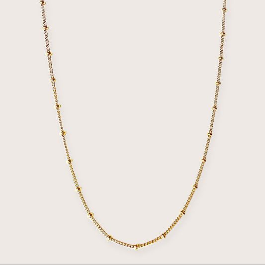 Vew of a 14K gold-filled beaded satellite station necklace featuring delicate curb chain links and evenly spaced round station beads against a neutral background