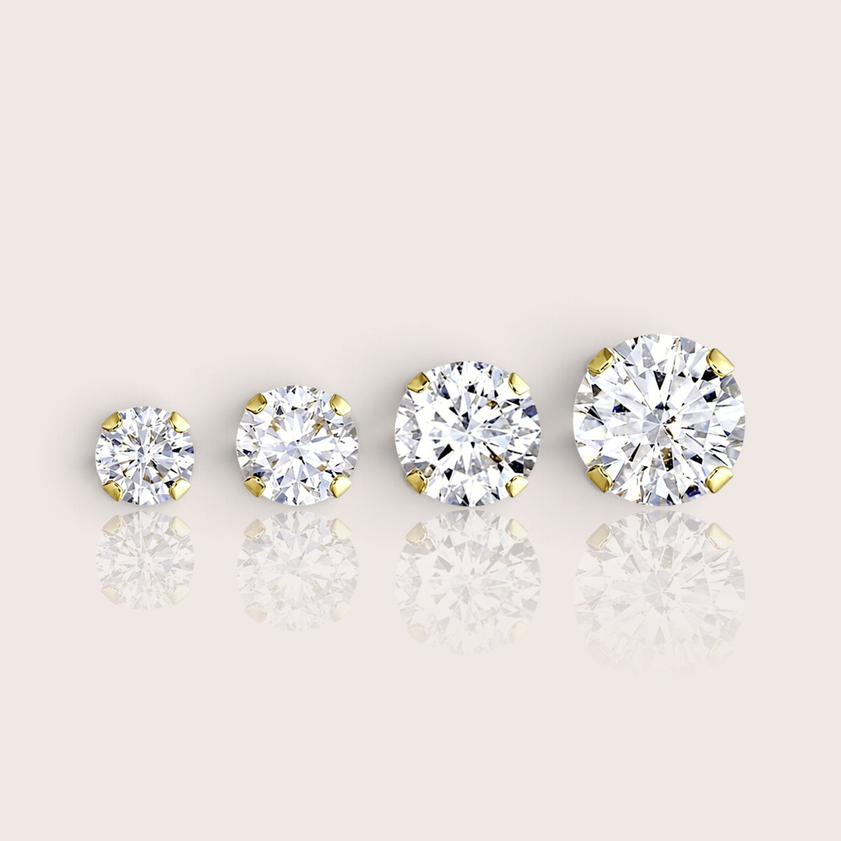 Four gold-filled solitaire CZ studs arranged from smallest to largest, showing four-prong settings on an ivory surface.