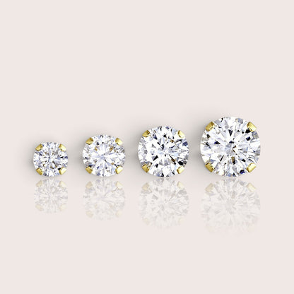 Four gold-filled solitaire CZ studs arranged from smallest to largest, showing four-prong settings on an ivory surface.
