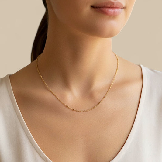 Close-up studio portrait of a model wearing a single delicate 14K gold-filled beaded satellite station necklace resting along her collarbone