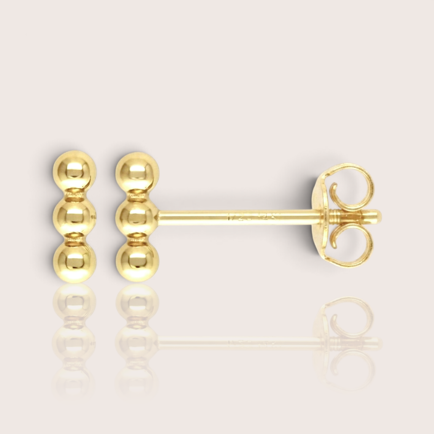 Close-up profile 14K gold-filled triple bead vertical bar stud earrings, display the minimalist, delicate gold cluster stud. The background is a soft, minimalist studio setting