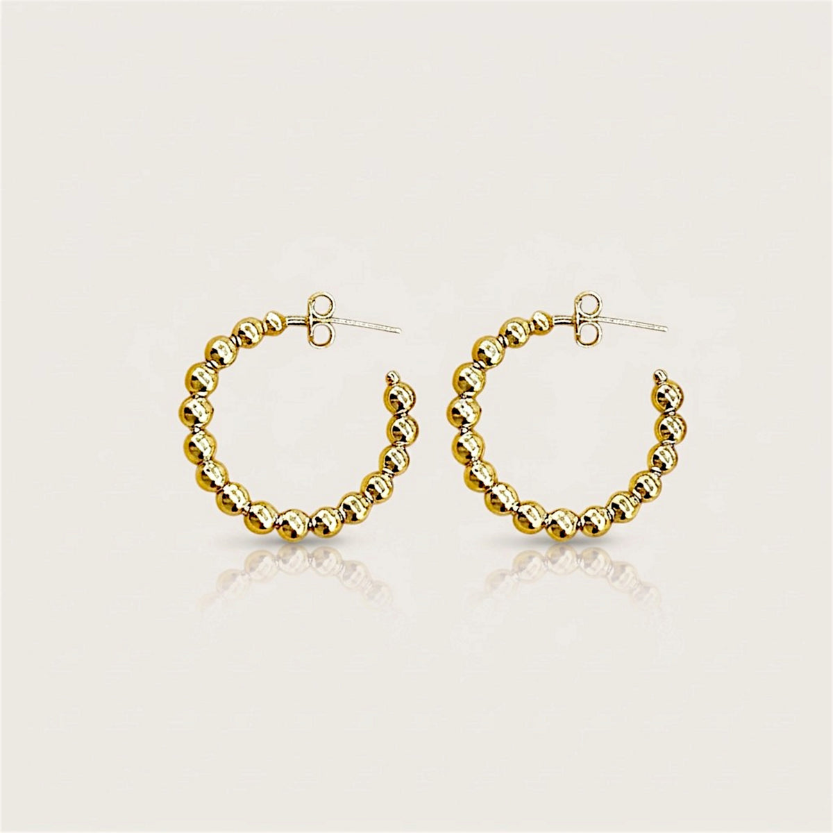 Pair of gold beaded C-shaped hoop earrings with butterfly backs on a neutral surface with soft reflections.