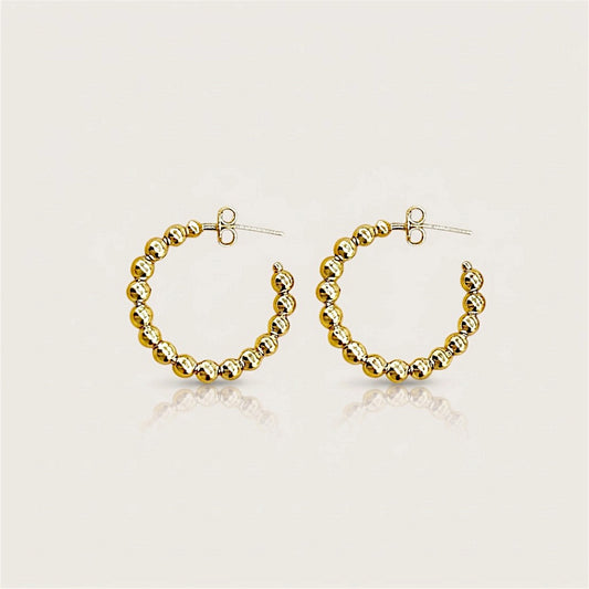 Pair of gold beaded C-shaped hoop earrings with butterfly backs on a neutral surface with soft reflections.