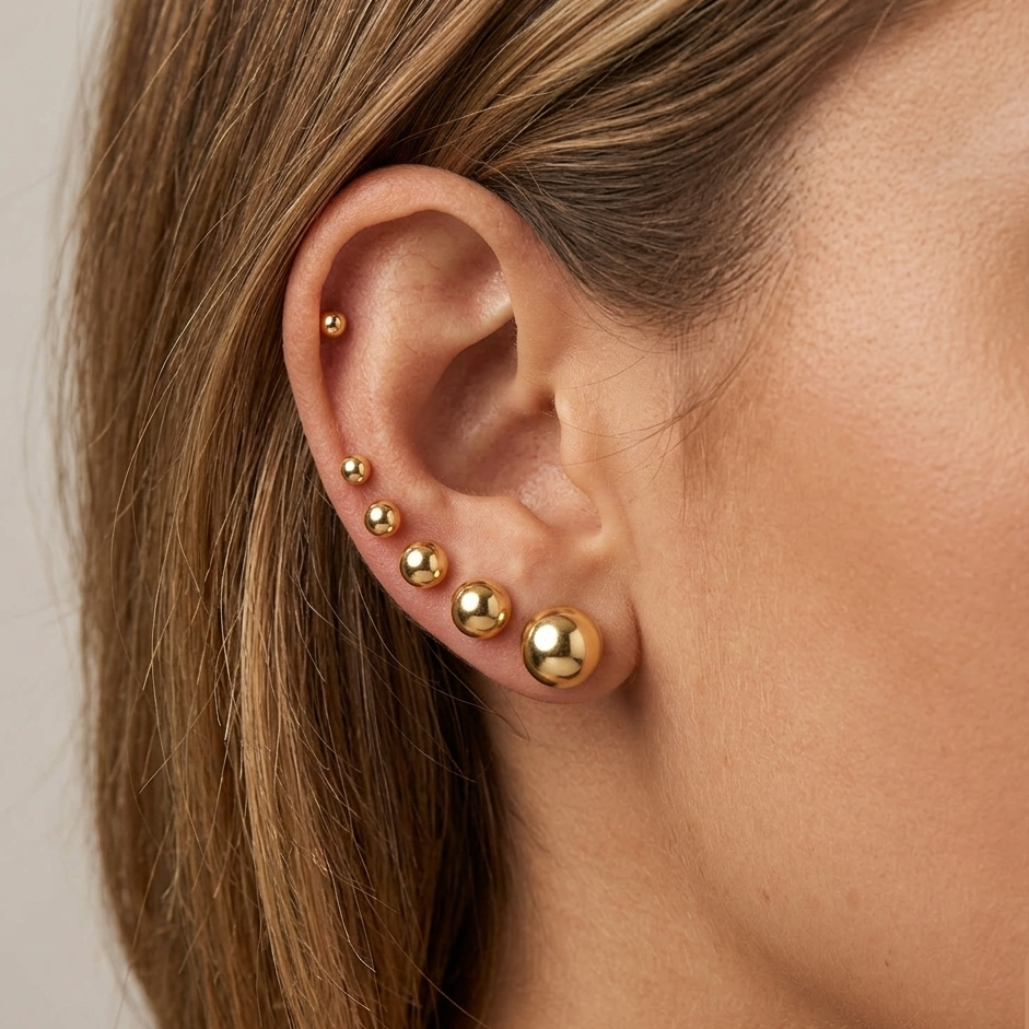 A styled ear stack showcasing the dainty 2mm -8mm gold-filled ball studs worn together in secondary and helix piercings on a model.s