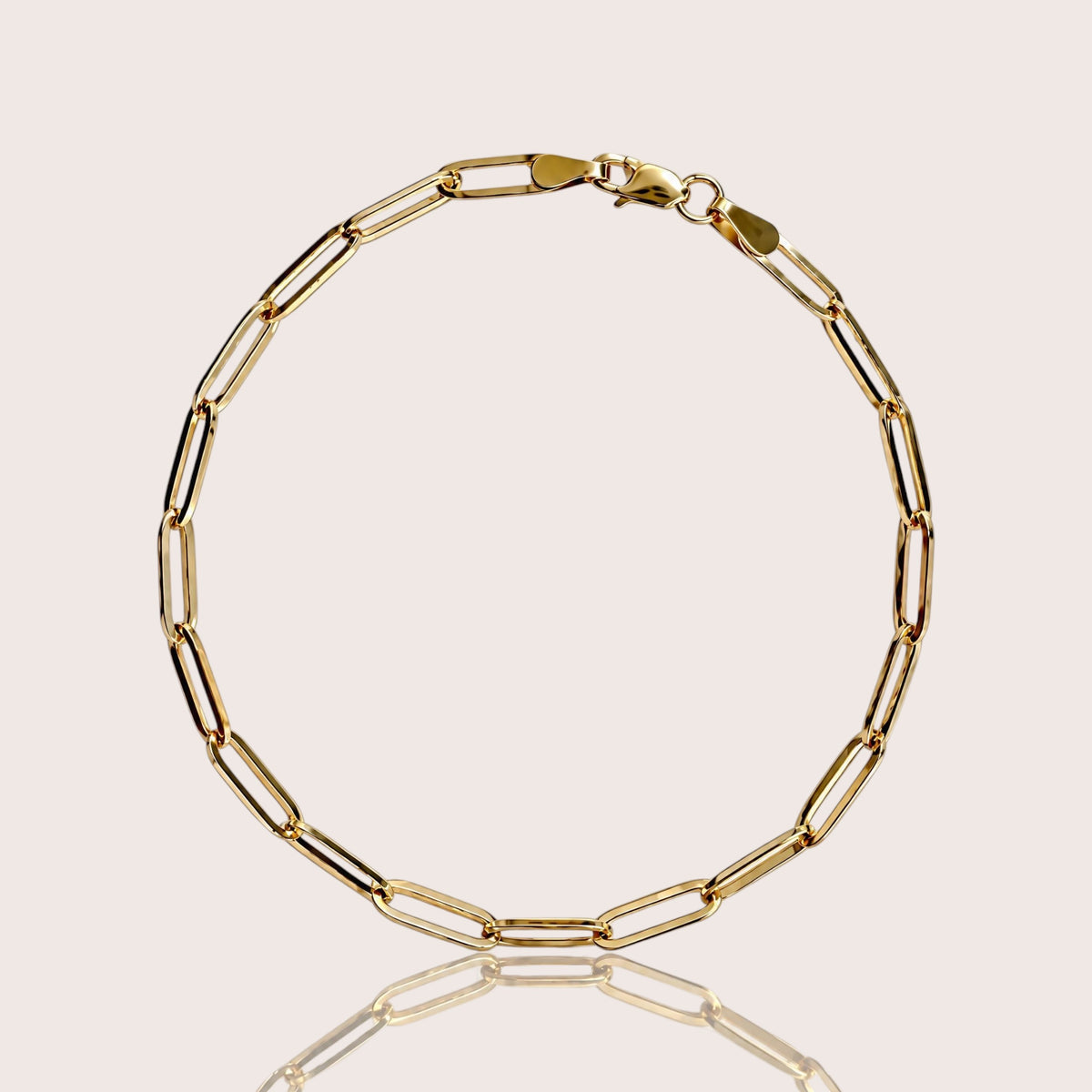 Solid 14K yellow gold paperclip link bracelet on a light beige background