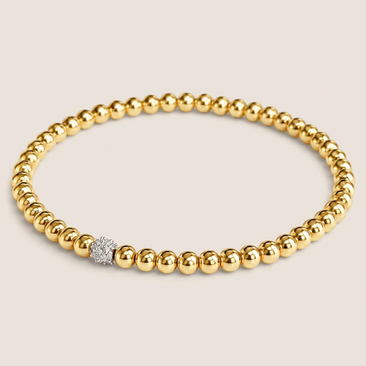 Polished gold bead stretch bracelet with a diamond accent bead, shown at an angle on an ivory background