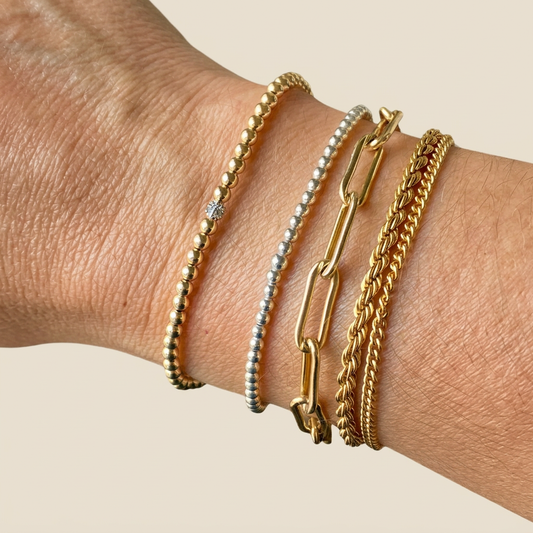 Gold diamond bead bracelet worn beside a silver beaded bracelet, gold paperclip bracelet, and gold chains