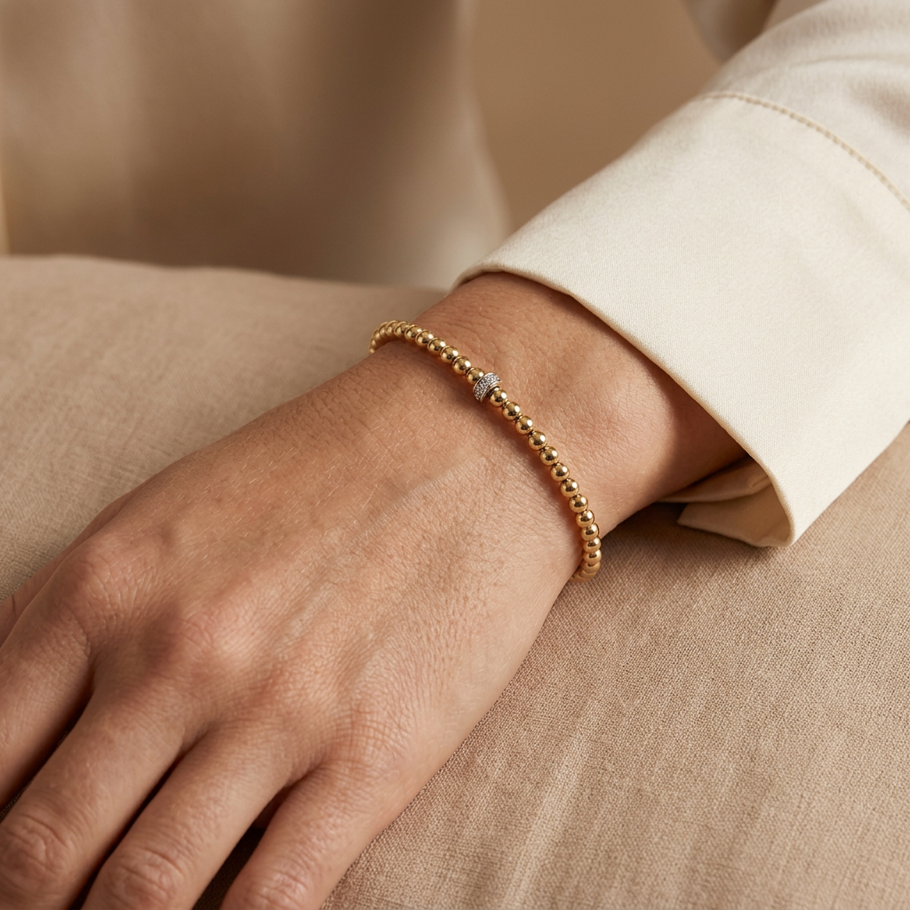Gold beaded bracelet with a diamond-set accent worn on a wrist beside an ivory shirt cuff