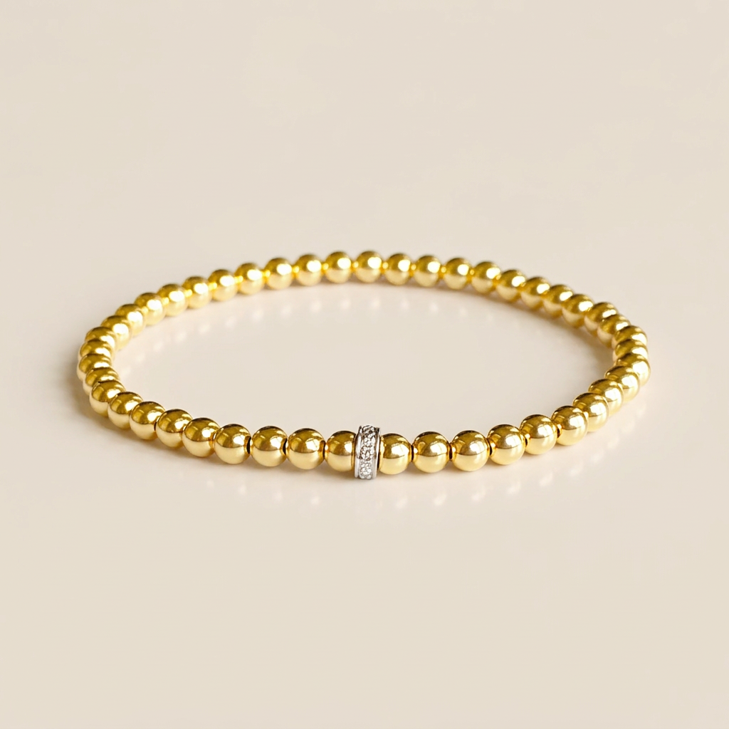 Yellow gold beaded bracelet with a narrow diamond-set accent resting on a warm beige background