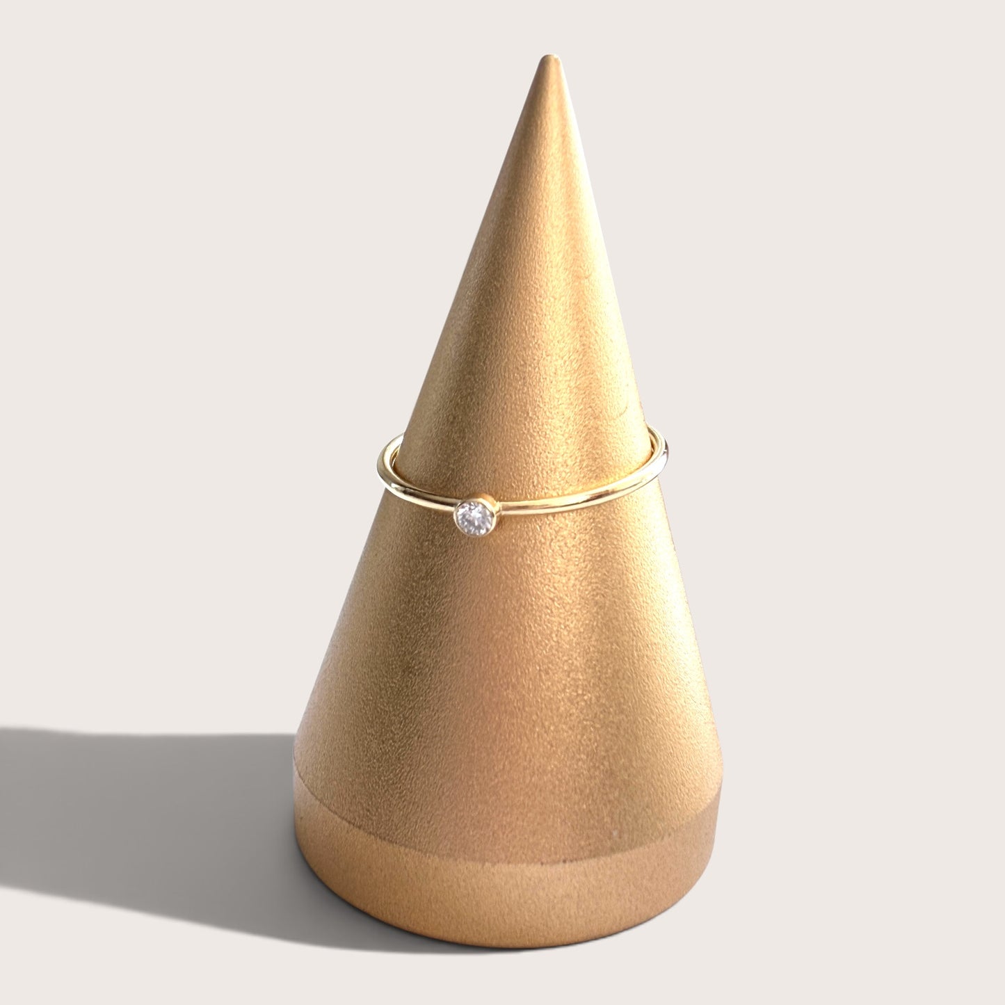 14K gold filled 2.0mm lab grown diamond bezel solitaire ring resting on a neutral linen jewelry display stand