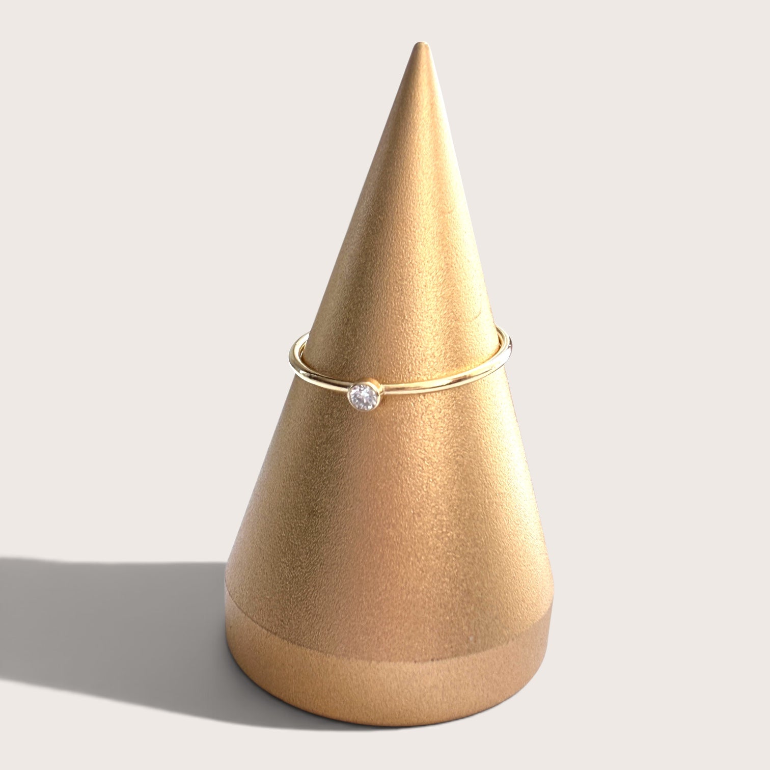 14K gold filled 2.0mm lab grown diamond bezel solitaire ring resting on a neutral linen jewelry display stand