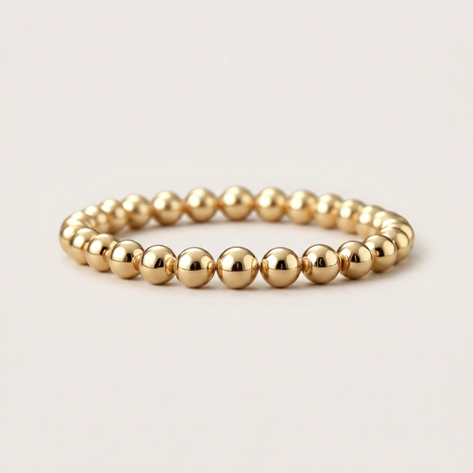 Polished gold-filled bead stretch bracelet shown at a low angle on an ivory background