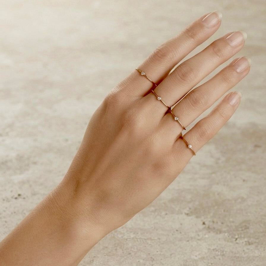 Model wearing gold filled rings on index, middle, ring, and pinky fingers featuring the 2.0mm lab diamond bezel solitaire
