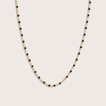 Black enamel bead satellite necklace on a fine gold-filled chain, arranged in a U shape on an ivory background.