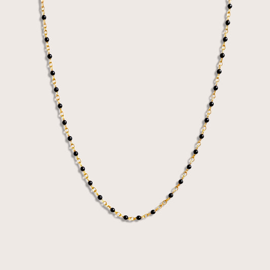 The 14K gold filled satellite necklace laid out flat on a premium neutral display, highlighting the gold chain links with black glossy enamel beads evenly stationed along the chain. 