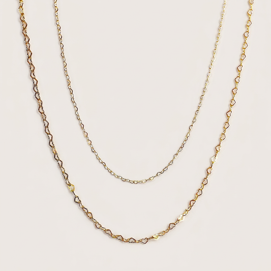 Mini and Small gold-filled heart chain necklaces arranged in nested curves on a beige background